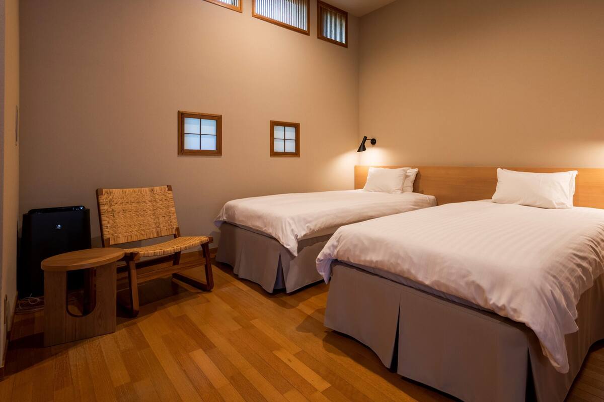 A hotel room with two beds, a small table, a chair, and a TV.