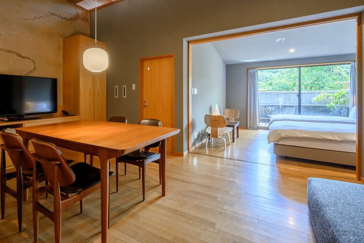 A modern interior with a dining area, a TV, and a bedroom with a large window.