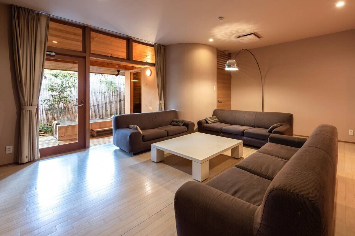 A modern living room with a sofa set, a coffee table, and a large window with a view of a bamboo fence.