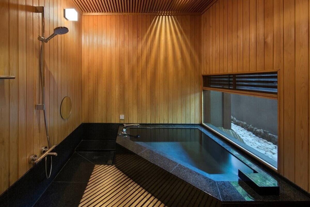 A wooden interior with a hot tub, a shower, and a window with a view of snow.