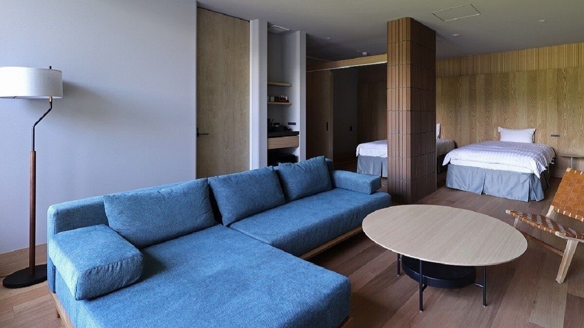 Moderni hotellihuone, jossa on sininen sohva, pyöreä pöytä, puinen päätyosalla varustettu sänky ja vaatekaappi.