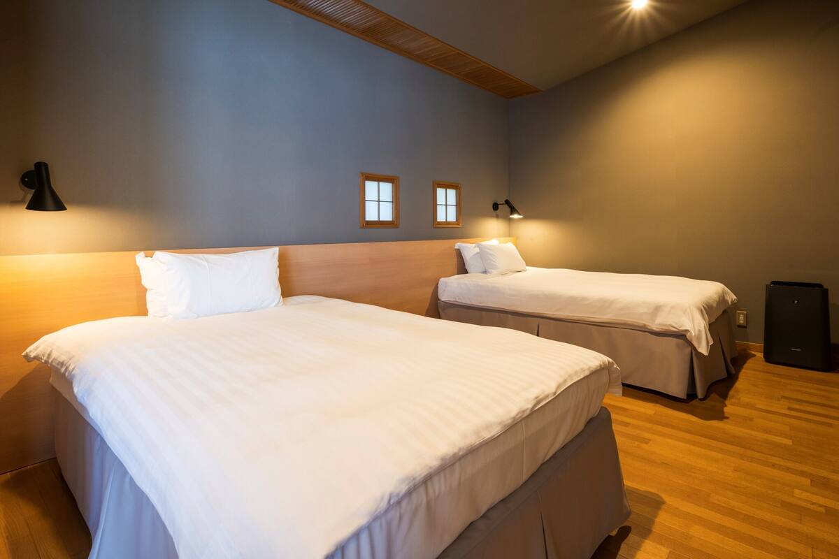 A hotel room with two beds, a wooden ceiling, a wall-mounted TV, and a small speaker.