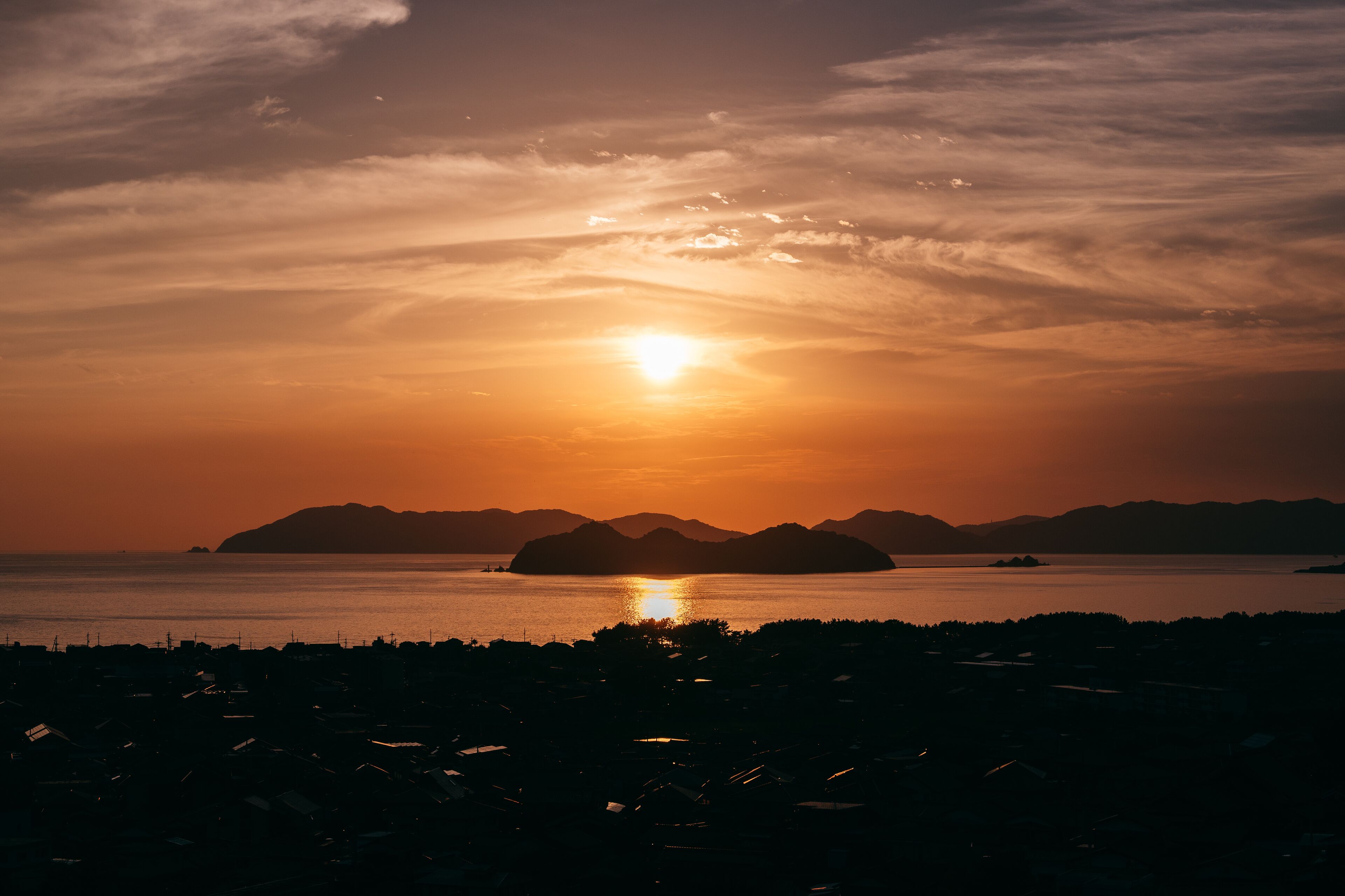 A sunset over a body of water with distant landforms.