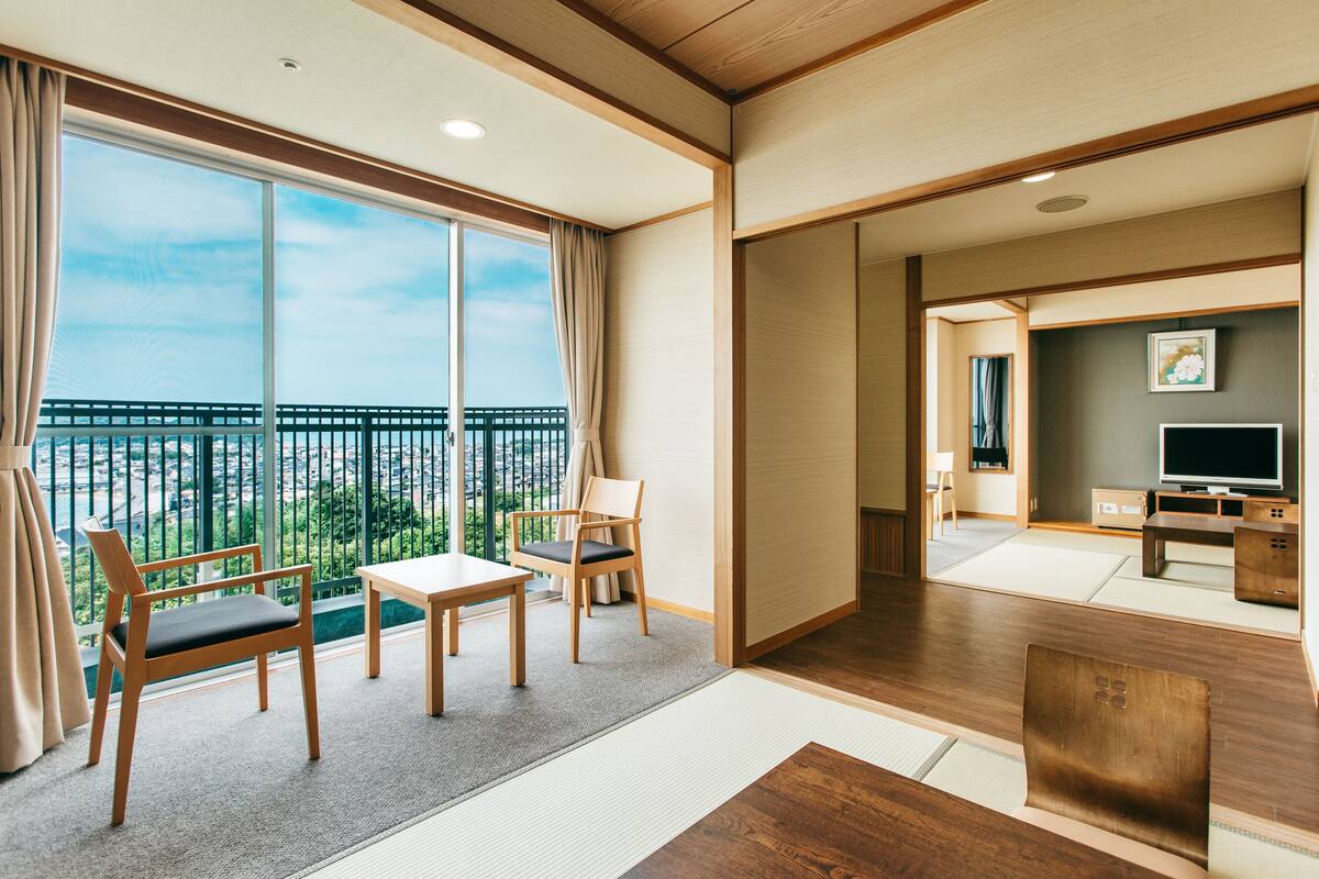 A modern hotel room with a large balcony, wooden furniture, and a television.