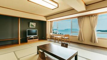 Una habitación moderna con suelo de tatami, una mesa de madera, sillas, un televisor y vista al mar.
