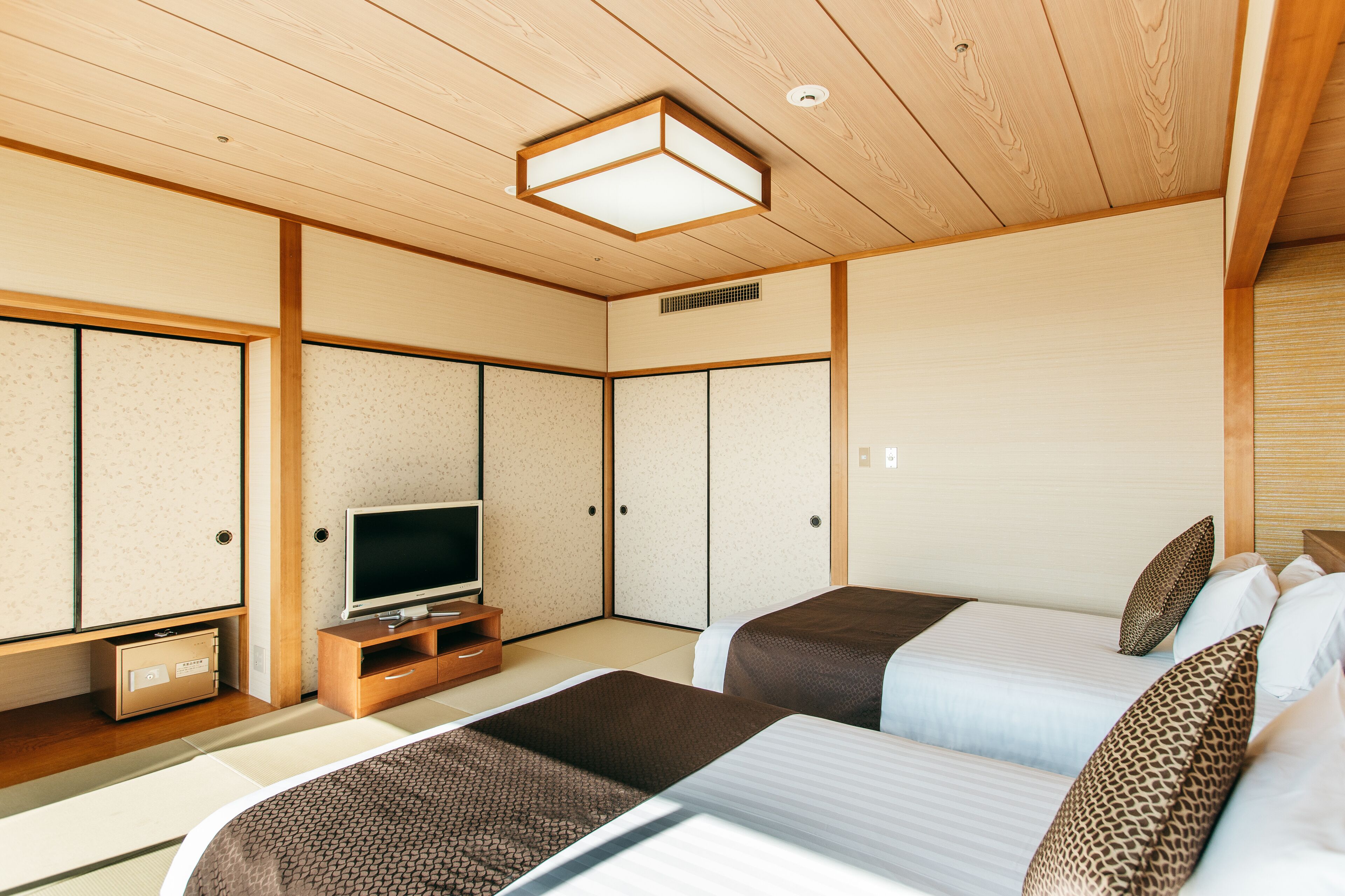 Una habitación tradicional japonesa con suelo de tatami, un televisor sobre un soporte de madera y dos camas con ropa de cama estampada.