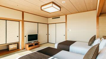 Una habitación tradicional japonesa con suelo de tatami, un televisor sobre un soporte de madera y dos camas con ropa de cama estampada.