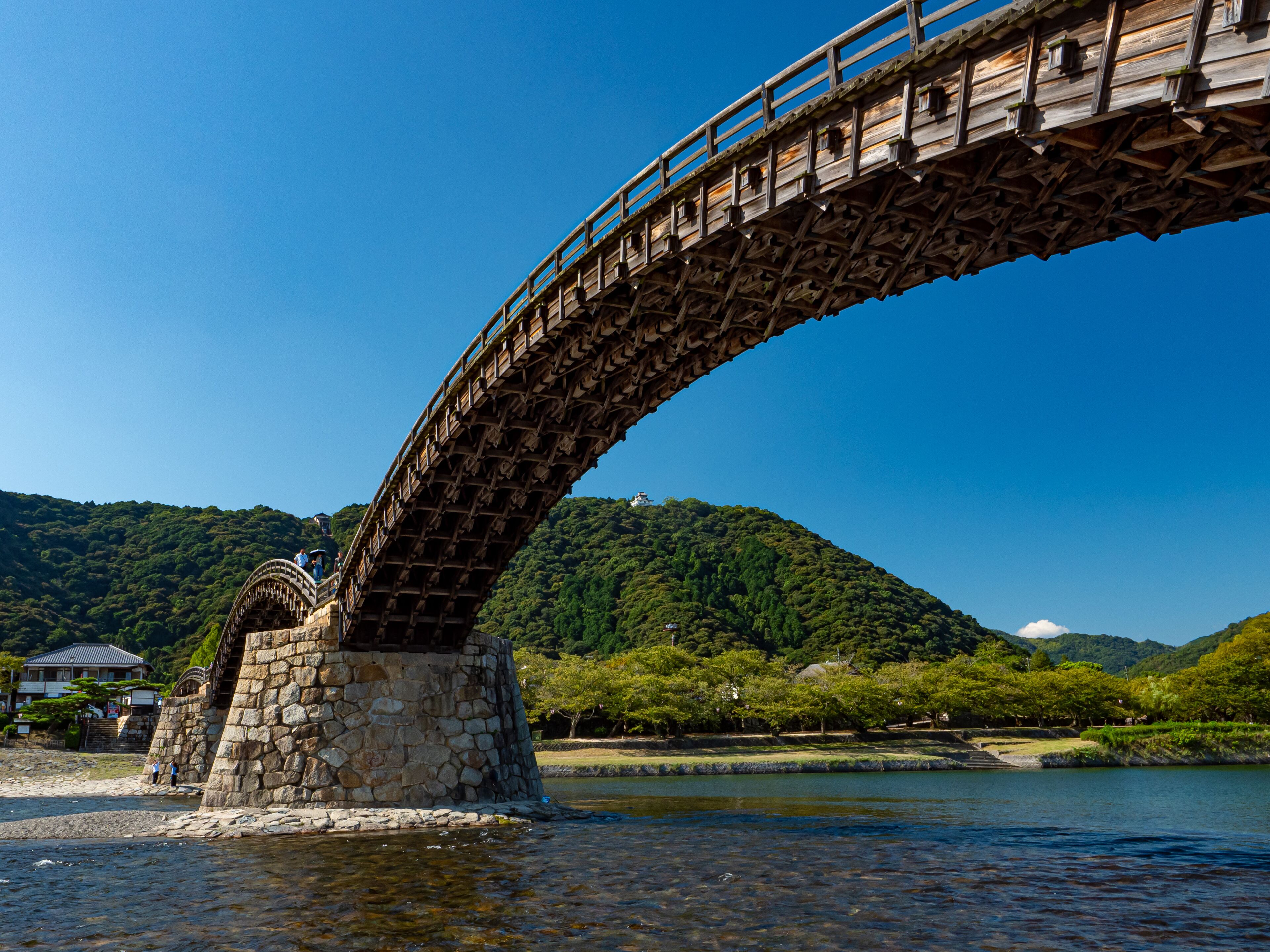 A stone bridge over a river with a forested hill in the background.
