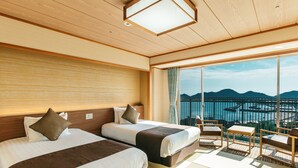 Ein Hotelzimmer mit zwei Betten, einem Balkon mit Blick auf das Meer und die Berge sowie einer kleinen Sitzecke.