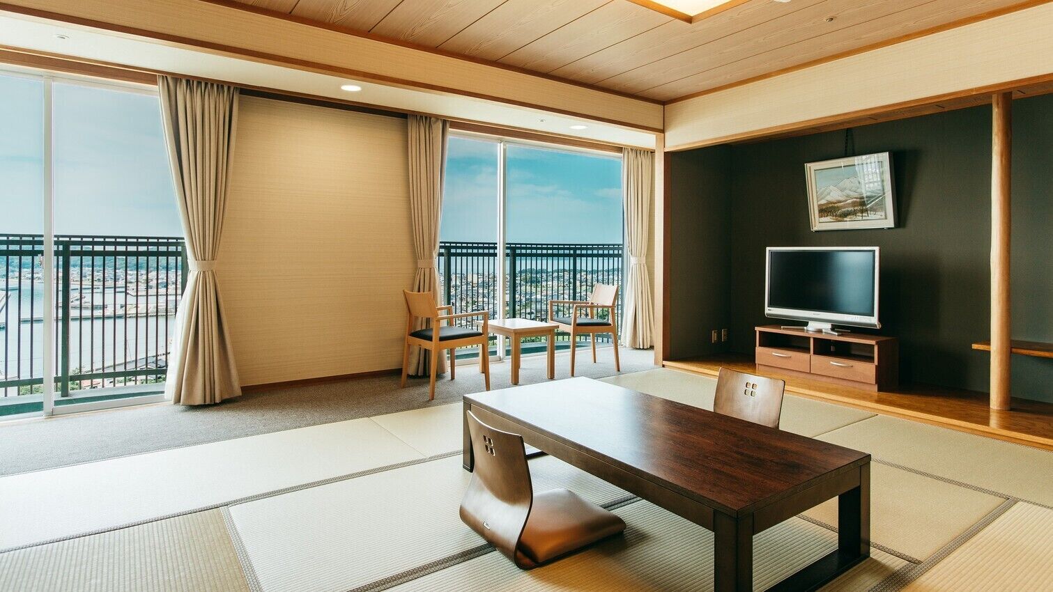 Een moderne hotelkamer met een groot raam, een eettafel, een televisie en een balkon met uitzicht.