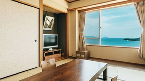 Ein Zimmer mit einem Holztisch, Stühlen, einem Fernseher und einem Fenster mit Meerblick.