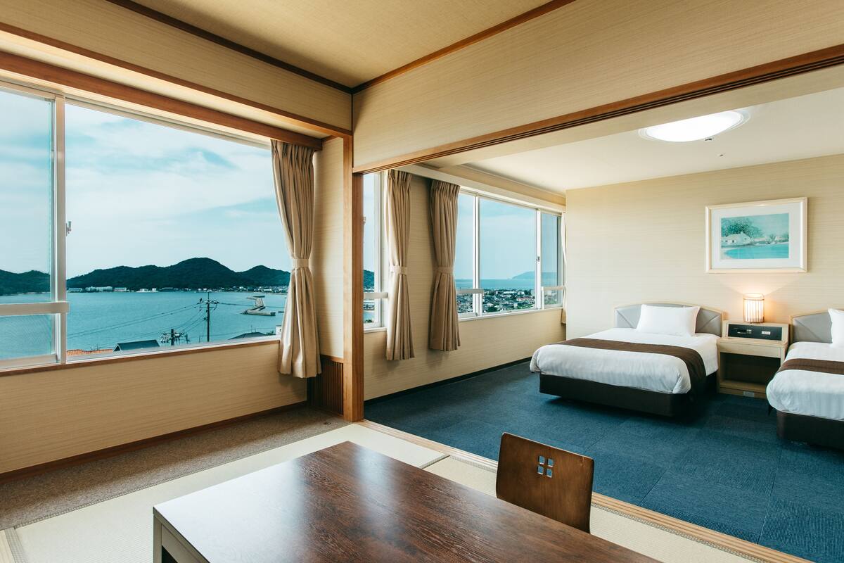 A hotel room with a large window, two beds, a table, and a chair.
