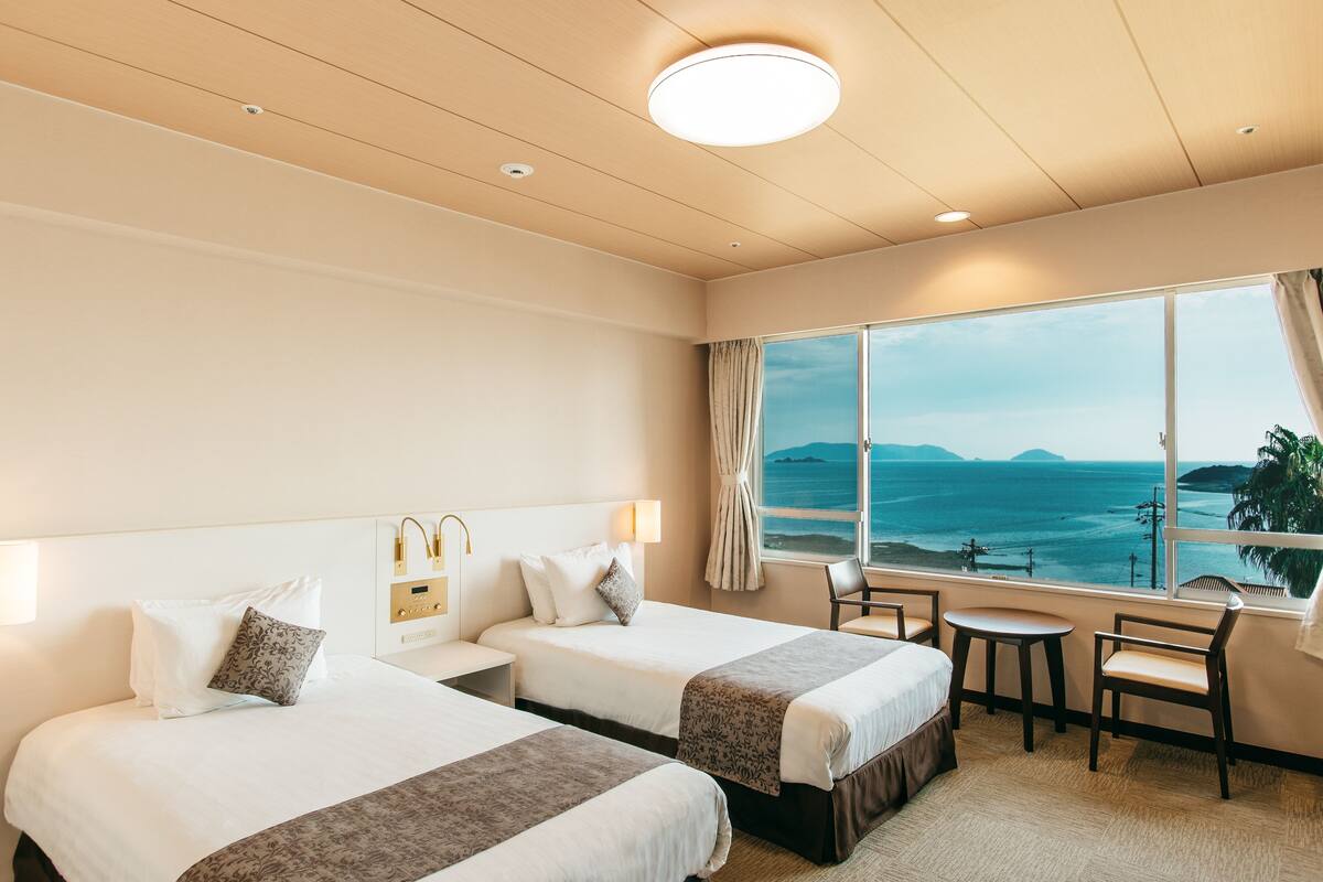A hotel room with two beds, a small table, and a view of the ocean.