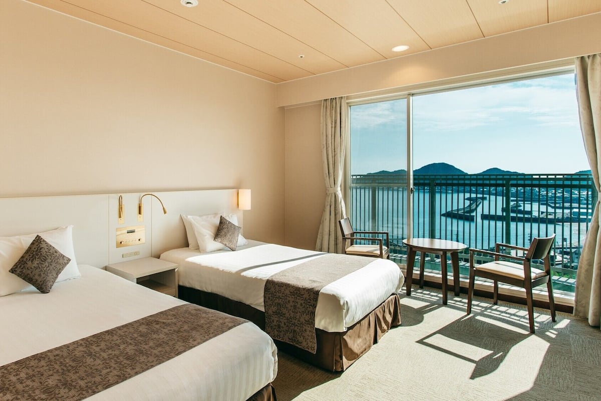 Ett hotellrum med två sängar, ett litet bord, en stol och en balkong med utsikt över havet.