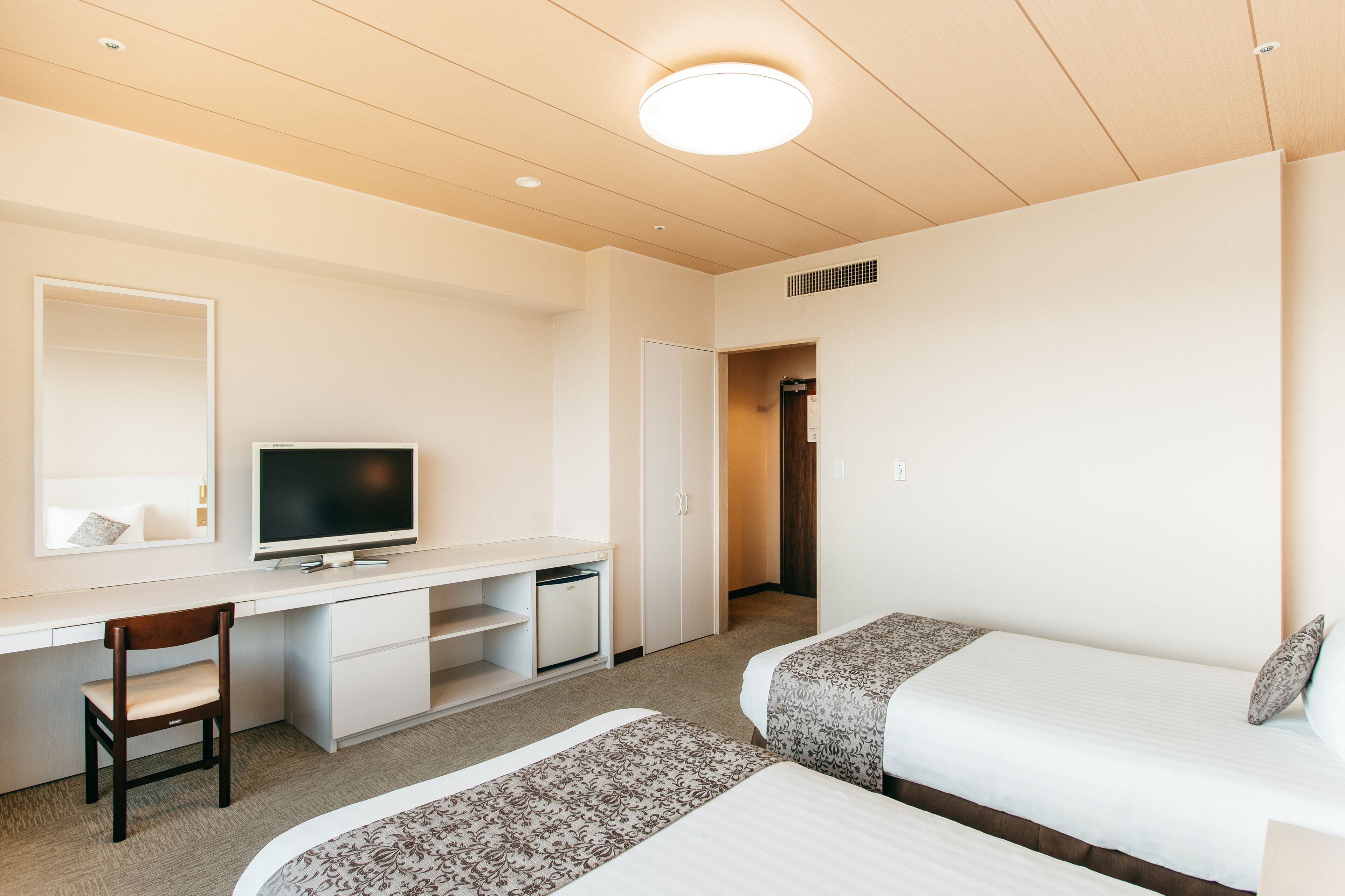 A hotel room with a desk, two beds, a television, and a wardrobe.