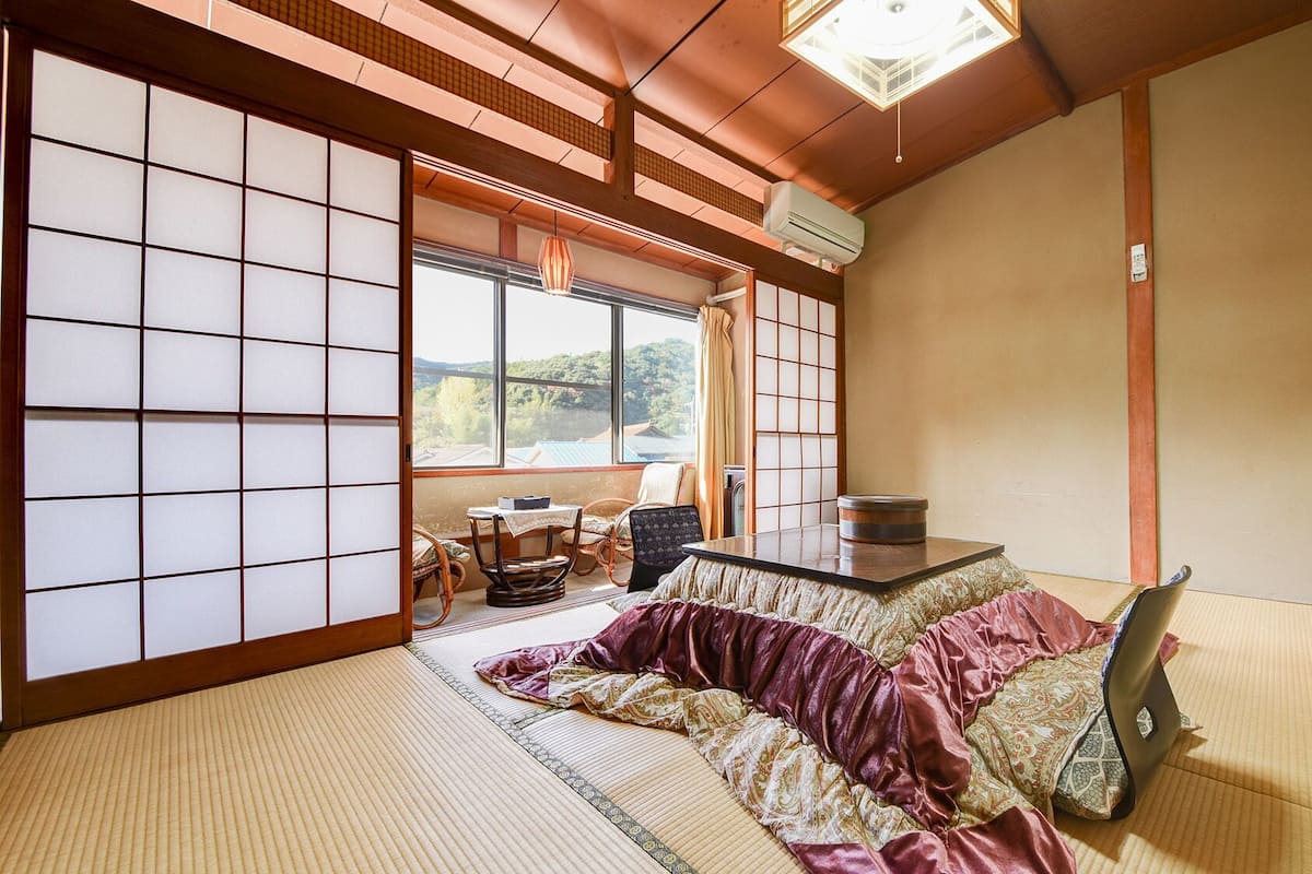 A traditional Japanese room with tatami flooring, a futon bed, a low table with a tea set, and a sliding shoji screen.