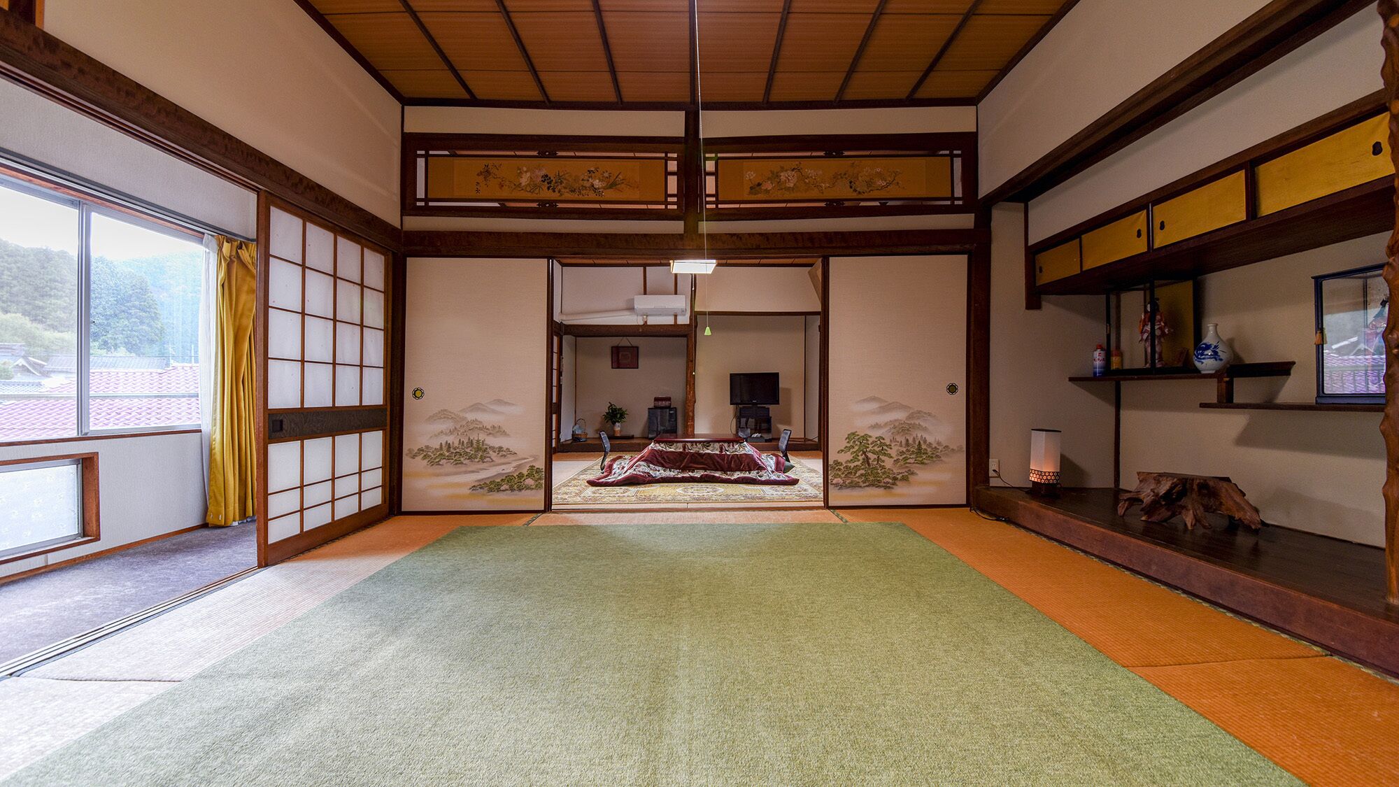 Una habitación tradicional japonesa con suelo de tatami, puertas correderas, un televisor y un biombo decorativo.