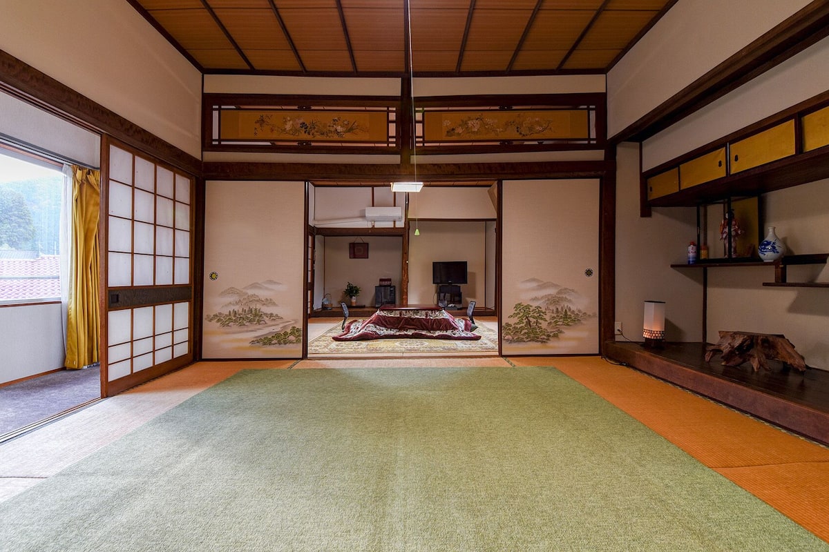 A traditional Japanese room with tatami flooring, sliding doors, a television, and a decorative screen.
