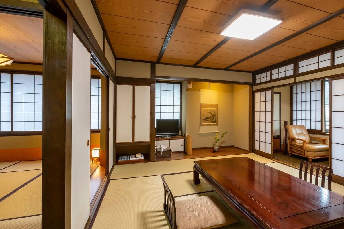 Et traditionelt japansk rum med tatamimåtter, et træbord, et fjernsyn og skydedøre.