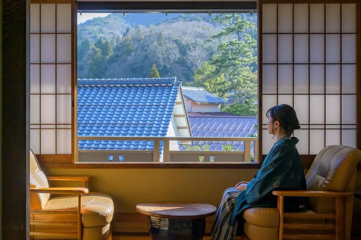 Una habitación japonesa tradicional con suelo de tatami, una mesa de madera baja y vistas a una montaña y edificios tradicionales.