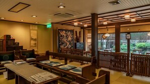 A traditional Japanese restaurant interior with tatami mat seating, low tables, and a view of a garden through large windows. - Iwai Onsen Iwaiya (Iwami)