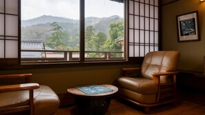 A room with a view of mountains, a leather chair, a wooden table, and a framed picture on the wall. - Iwai Onsen Iwaiya (Iwami)