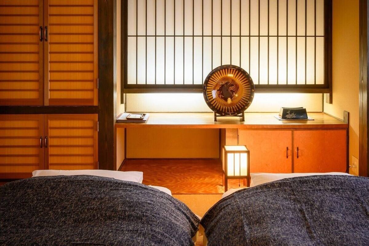 Et traditionelt japansk rum med skydedøre, en gulv belagt med tatami-måtter, et lavt bord med en dekorativ tallerken og et lille natbord med en lampe.