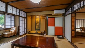 A traditional Japanese room with tatami flooring, a low table, a cushioned chair, and sliding doors with a shoji screen. - Iwai Onsen Iwaiya (Iwami)