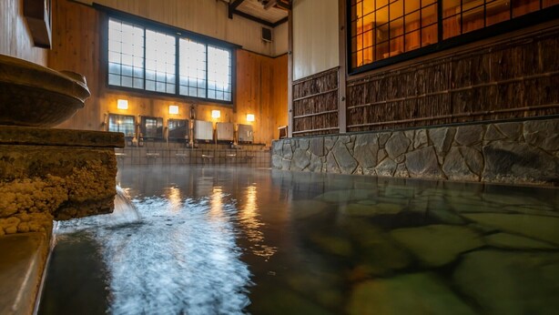 A hot spring area with stone walls, wooden beams, and a view of the interior. - Iwai Onsen Iwaiya (Iwami)