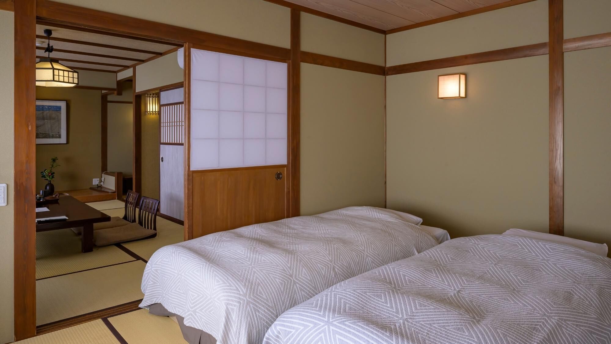 Una habitación tradicional japonesa con suelo de tatami, una cama baja de madera con ropa blanca, una puerta corredera shoji y un pequeño escritorio con una silla.