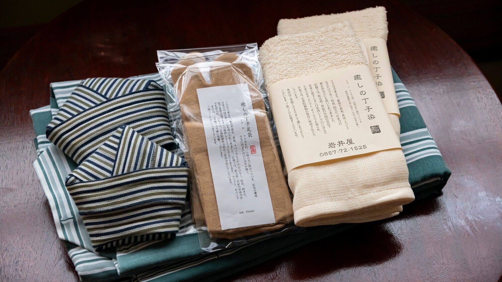 Una tela a rayas bien doblada, una toalla color beige y un papel con texto japonés sobre una mesa de madera.