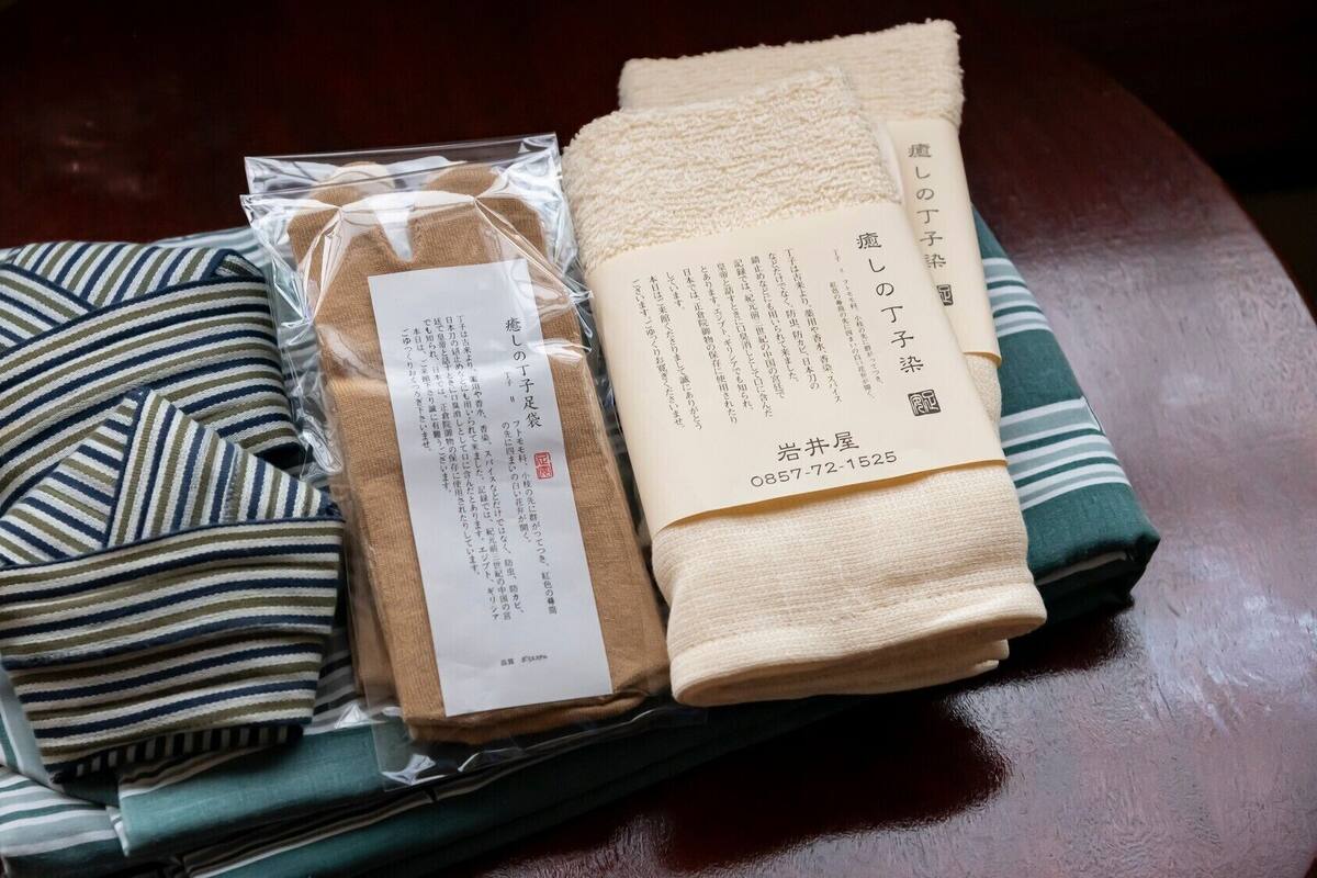 Et pænt foldet stribet stof, et beige håndklæde og et stykke papir med japansk tekst på et træbord.