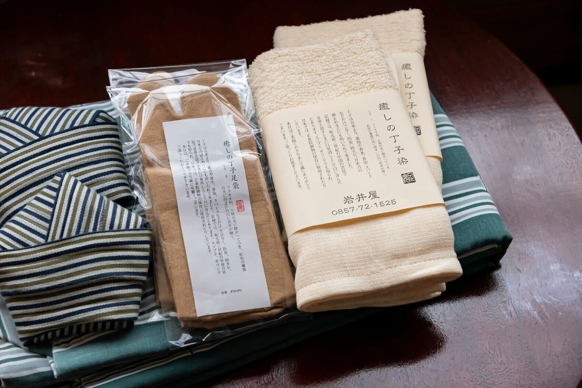 Una tela a rayas bien doblada, una toalla color beige y un papel con texto japonés sobre una mesa de madera.
