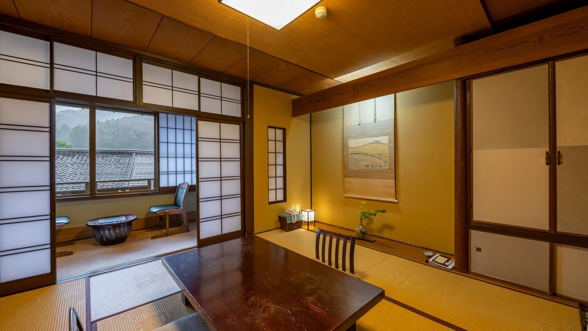 Una habitación japonesa tradicional con suelo de tatami, puertas correderas, una mesa de madera y vistas a la montaña.