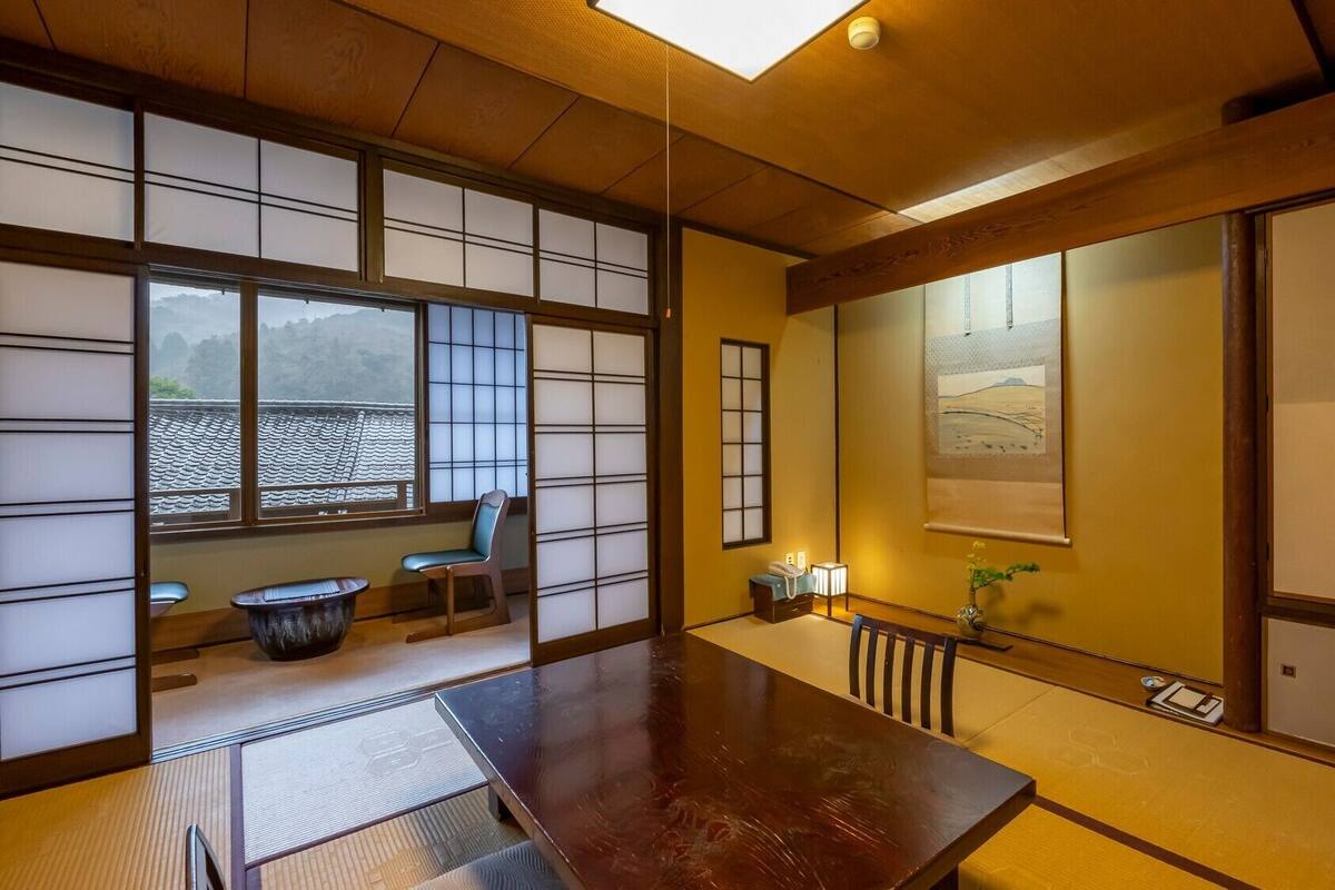Et traditionelt japansk rum med tatami-gulv, skydedøre, et træbord og udsigt til et bjerg.
