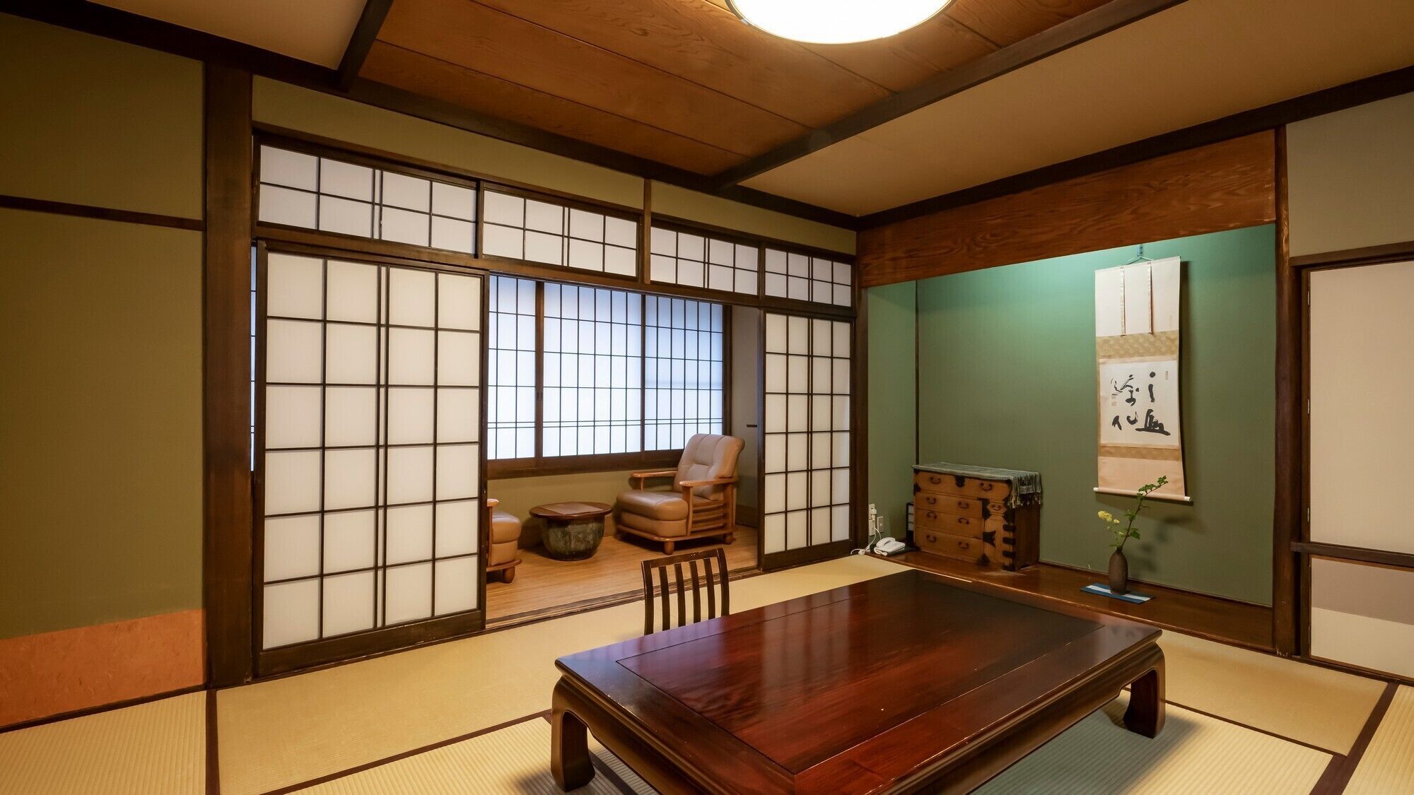 Una habitación japonesa tradicional con suelo de tatami, una mesa de madera baja, una silla acolchada y puertas correderas shoji.