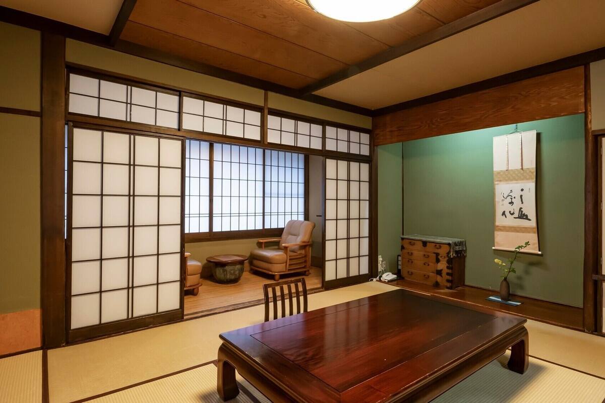 Et traditionelt japansk rum med tatamimåtter, et lavt træbord, en polstret stol og skydelåger i shoji-stil.