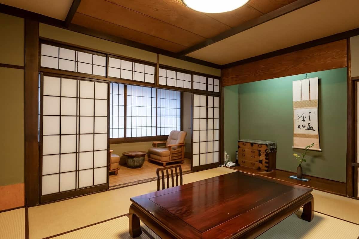 Una habitación japonesa tradicional con suelo de tatami, una mesa de madera baja, una silla acolchada y puertas correderas shoji.