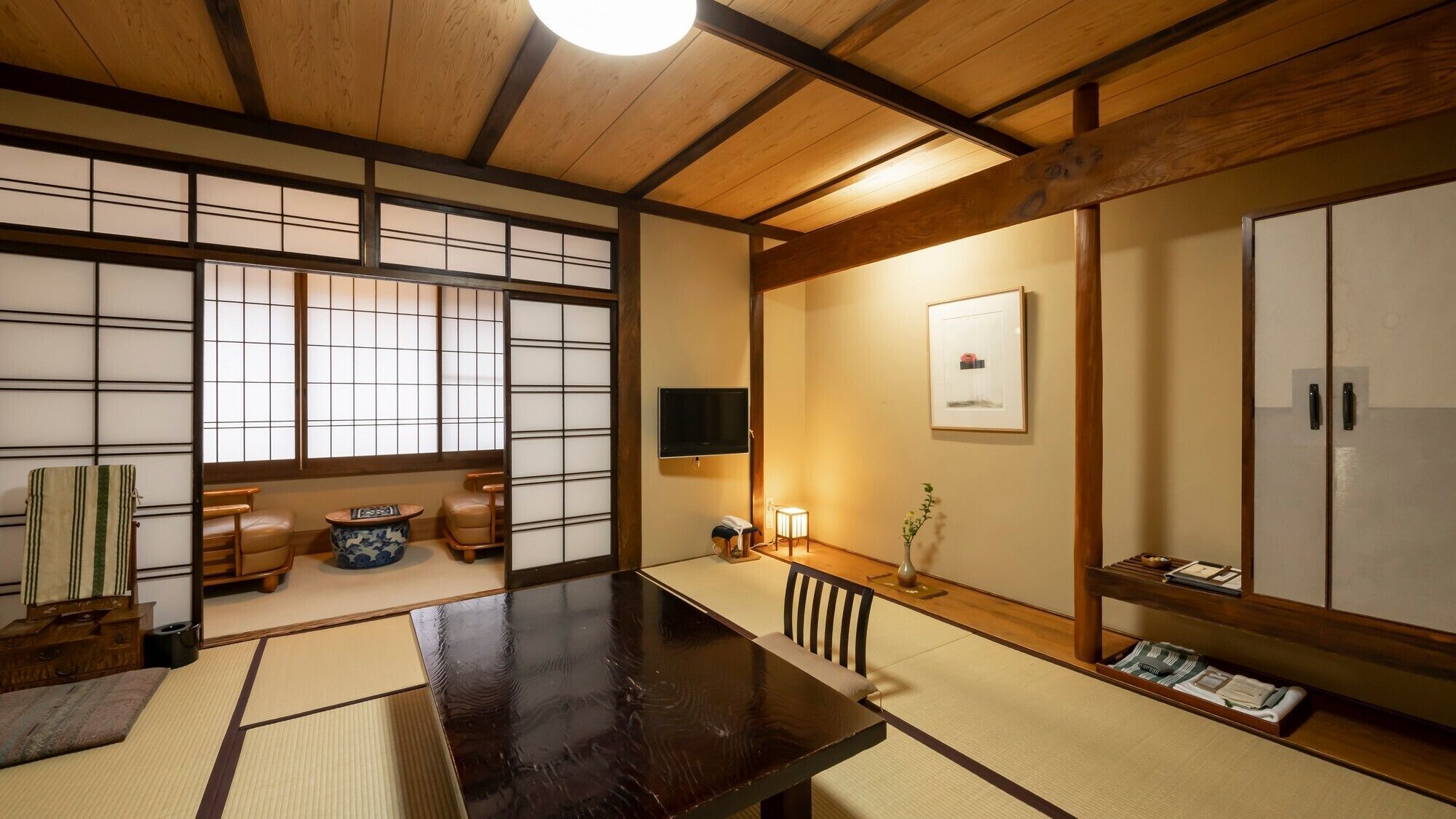 Una habitación japonesa tradicional con suelo de tatami, una mesa de madera oscura, puertas correderas y un televisor.