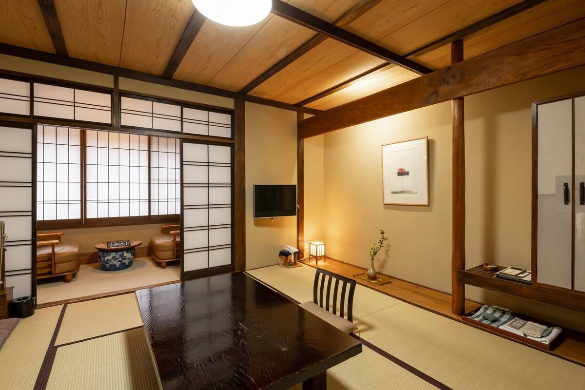 Et traditionelt japansk rum med tatamimåtter, et mørkt træbord, skydedøre og et fjernsyn.