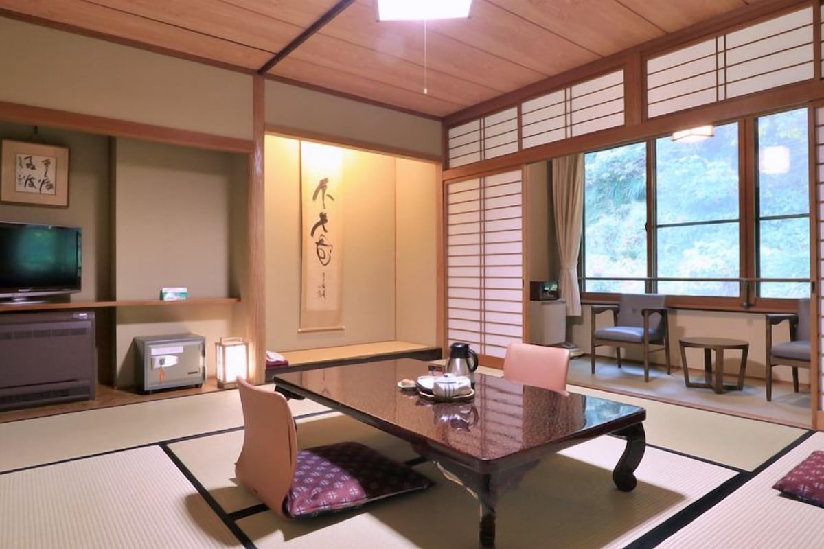 Une pièce de style japonais traditionnel, avec un sol recouvert de tatamis, un téléviseur, un radiateur, une table avec des coussins et une porte coulissante.
