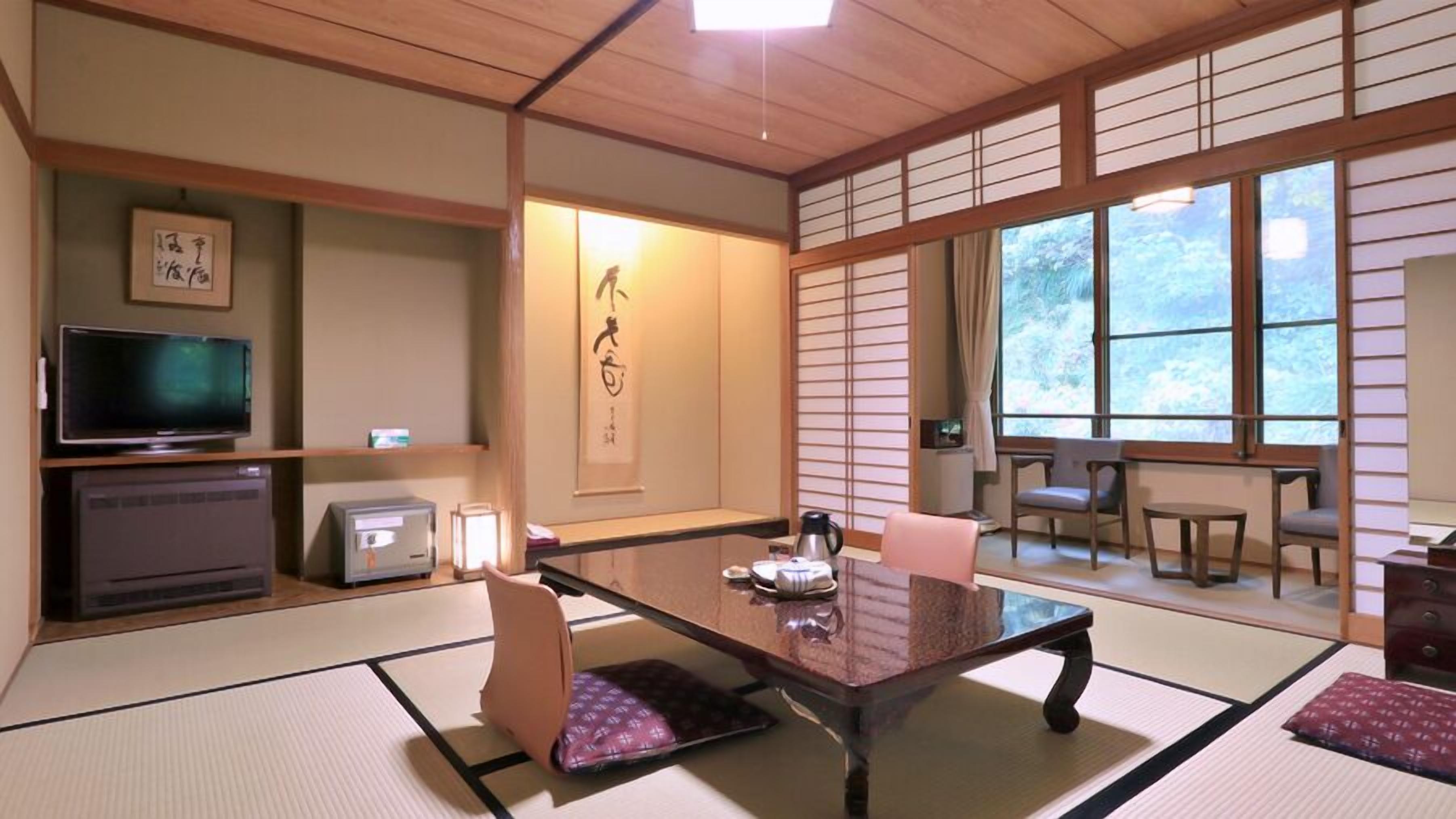 Una habitación japonesa tradicional con suelo de tatami, televisión, calentador, una mesa con cojines y una puerta corredera.