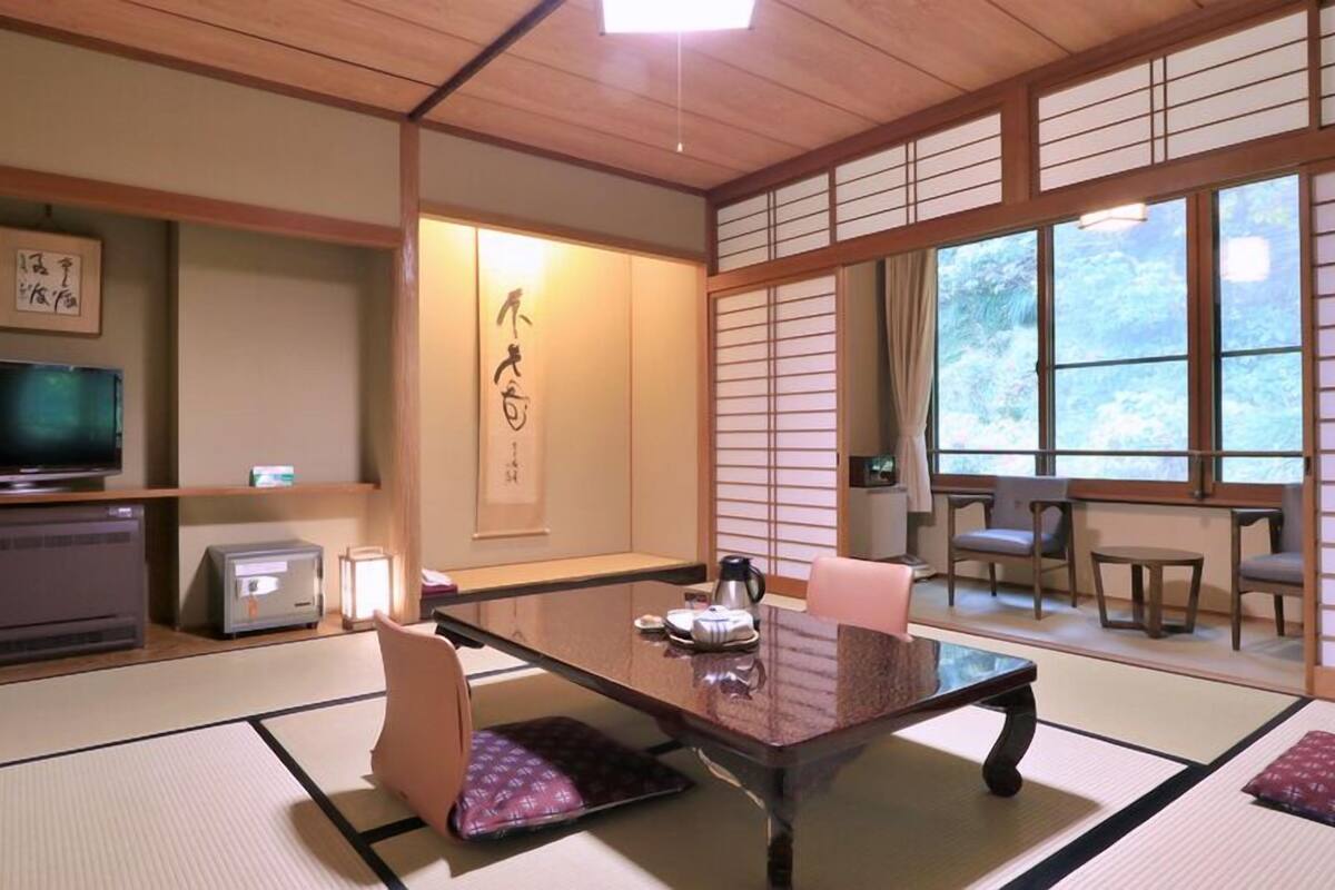 Une pièce de style japonais traditionnel, avec un sol recouvert de tatamis, un téléviseur, un radiateur, une table avec des coussins et une porte coulissante.