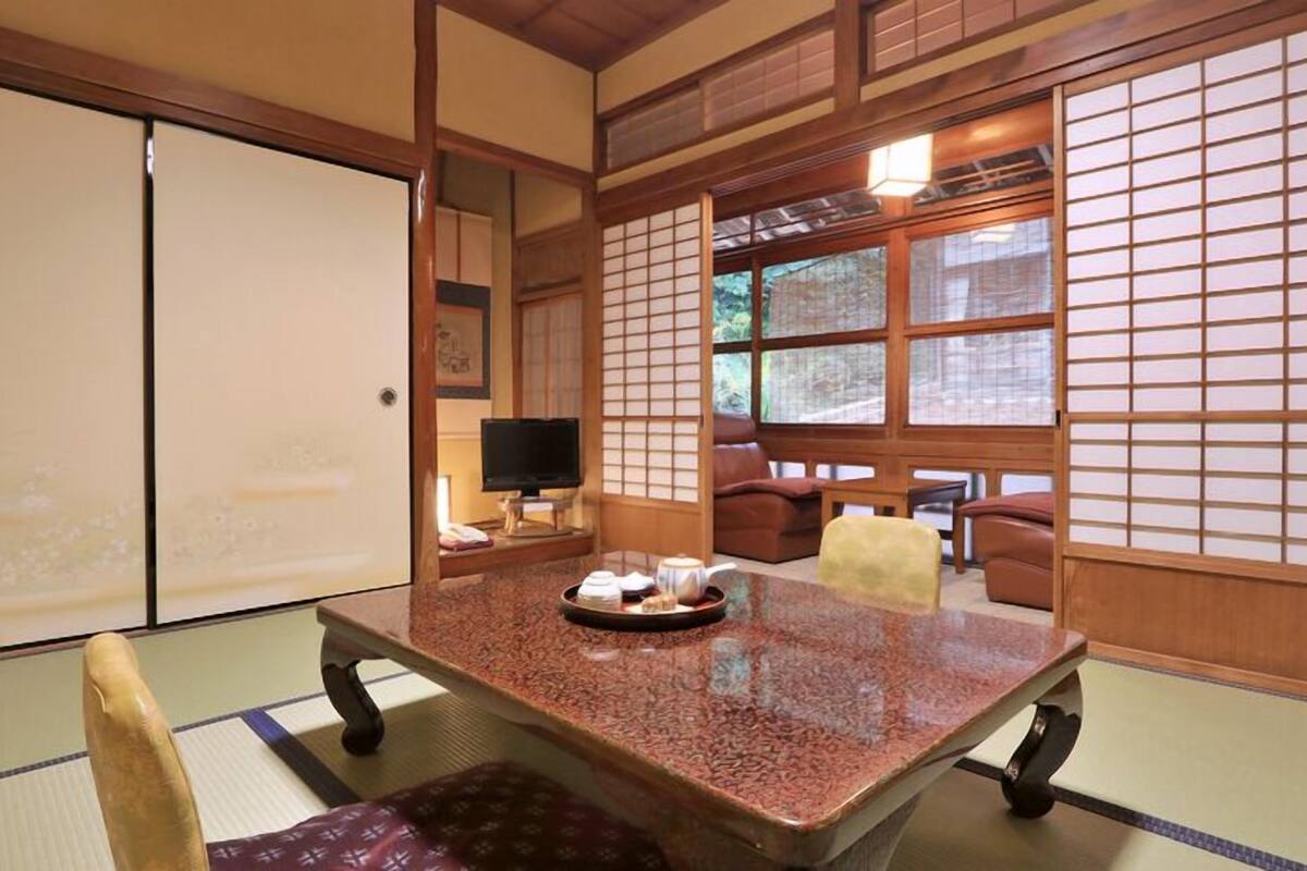 Une pièce de style japonais traditionnel, avec un sol recouvert de tatamis, une petite table basse sur laquelle est posée une théière, et des portes coulissantes.