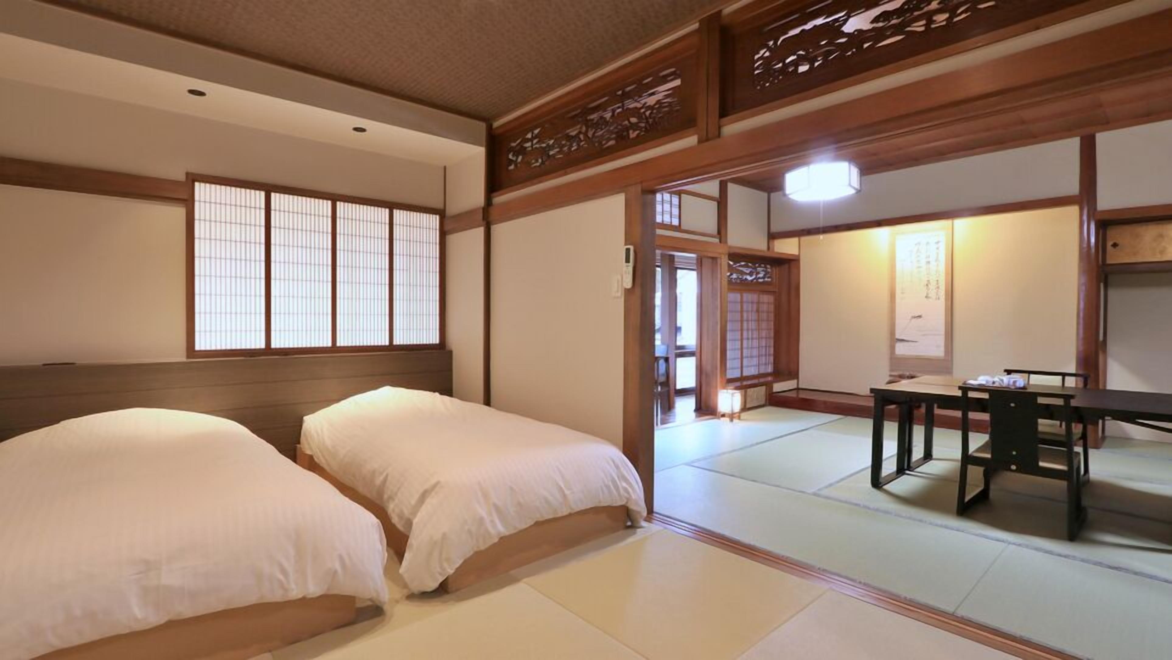 Una habitación japonesa tradicional con suelo de tatami, dos camas, una mesa y puertas correderas.