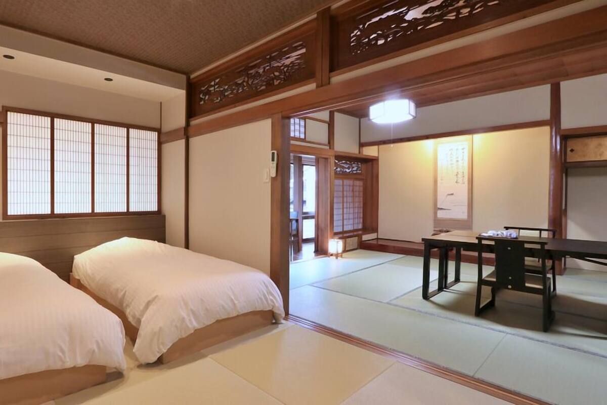 Une pièce de style japonais traditionnel, avec un sol recouvert de tatamis, deux lits, une table et des portes coulissantes.