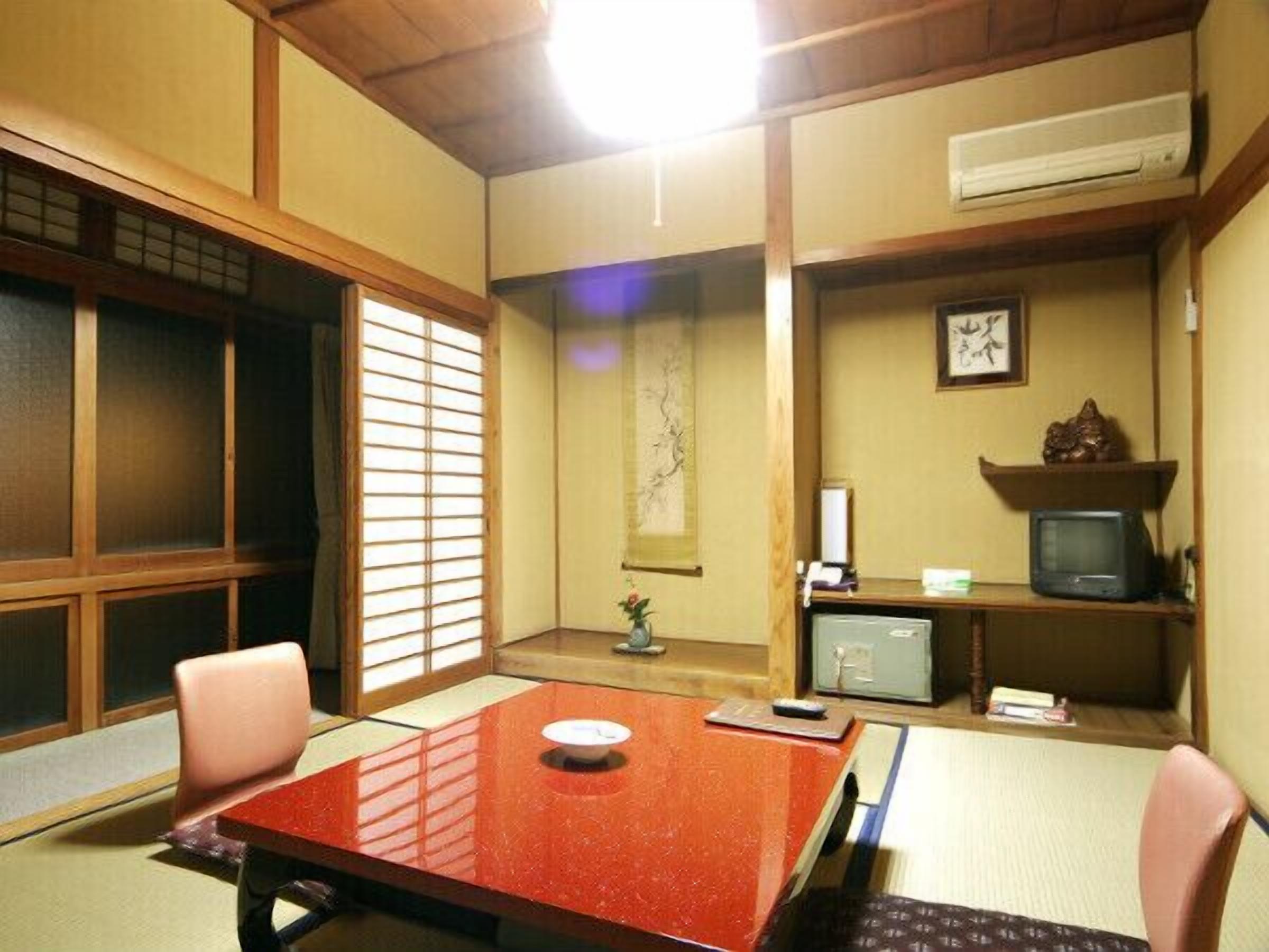 Ein traditioneller japanischer Raum mit Tatami-Böden, einem niedrigen Tisch und einem Fernseher auf einem Regal.