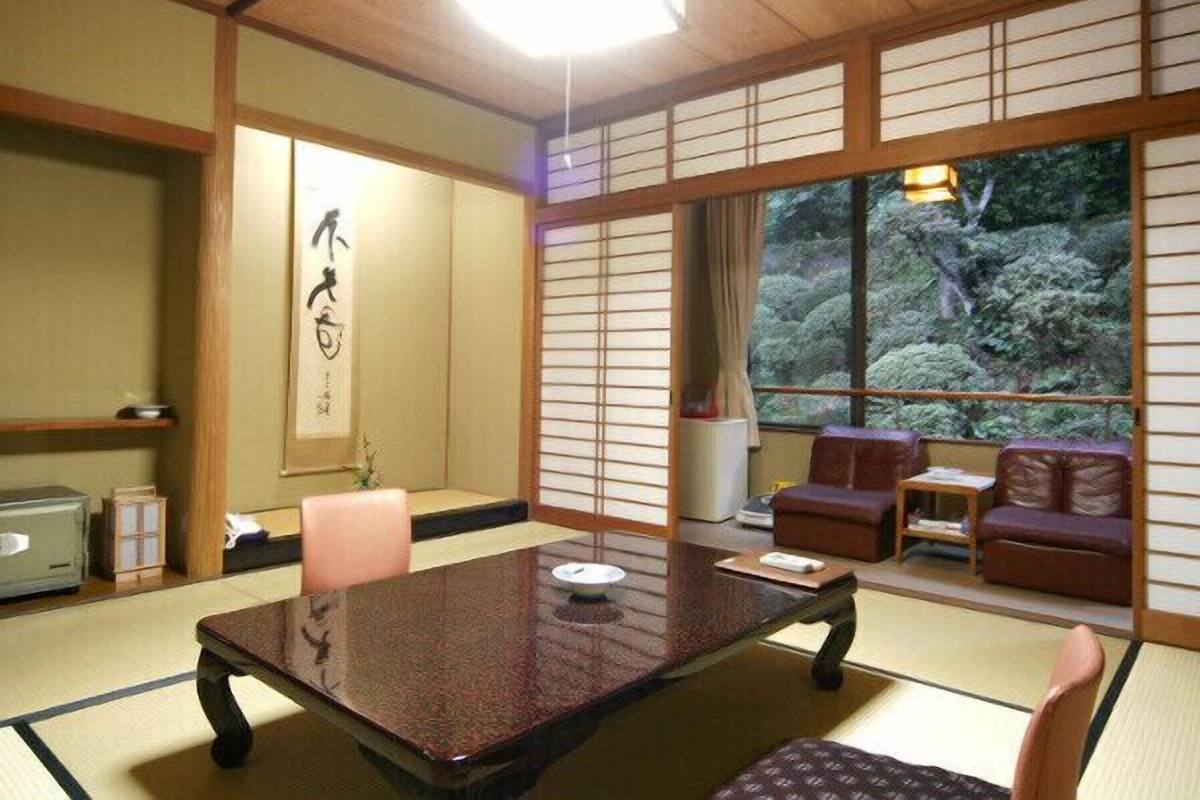 Une pièce de style japonais traditionnel, avec un sol recouvert de tatamis, une table basse et une vue sur la verdure environnante.