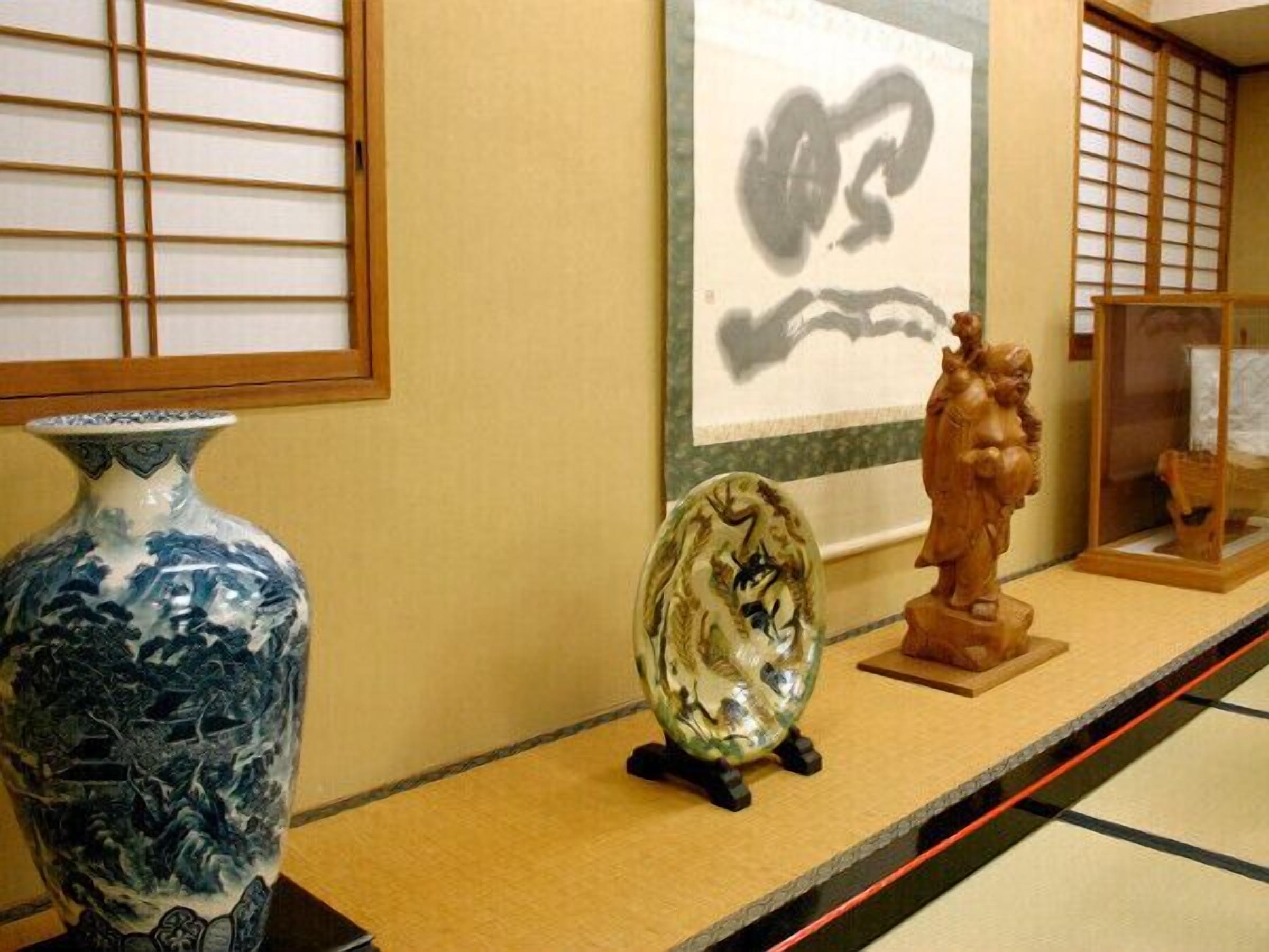 Eine Präsentation traditioneller japanischer Kunst, darunter eine Keramikvase, eine reflektierende Skulptur und ein gerahmtes Kunstwerk.