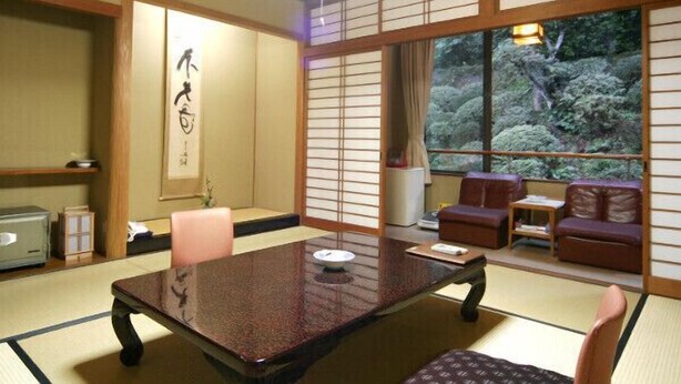 A traditional Japanese room with tatami flooring, a low table, and a view of greenery outside. - Yunotsu Onsen Nogawaya Ryokan (Oda)